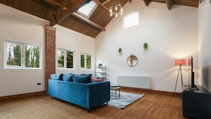 A spacious living room with a blue sofa, wooden flooring, a brick wall, and large windows.