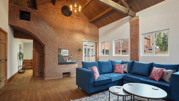 A cozy living room with a blue sofa, a fireplace, and a wooden staircase.
