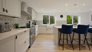 A modern kitchen with white cabinetry, a built-in oven, and a bar area with blue chairs.