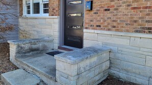 Una casa con puerta principal oscura, fachada de ladrillo y una pequeña escalera de piedra que conduce a la entrada.