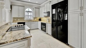 A modern kitchen with white cabinetry, a granite countertop, a black refrigerator, and a microwave. - Family fun by the beach! 5500 sq ft with 5 BRs, 5 baths, game room, heated pool (Destin)