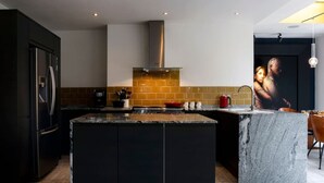 A modern kitchen with a central island, dark cabinetry, a stainless steel refrigerator, and a tiled backsplash. - Detached Edwardian Villa with Garden & Parking (Broadstairs)