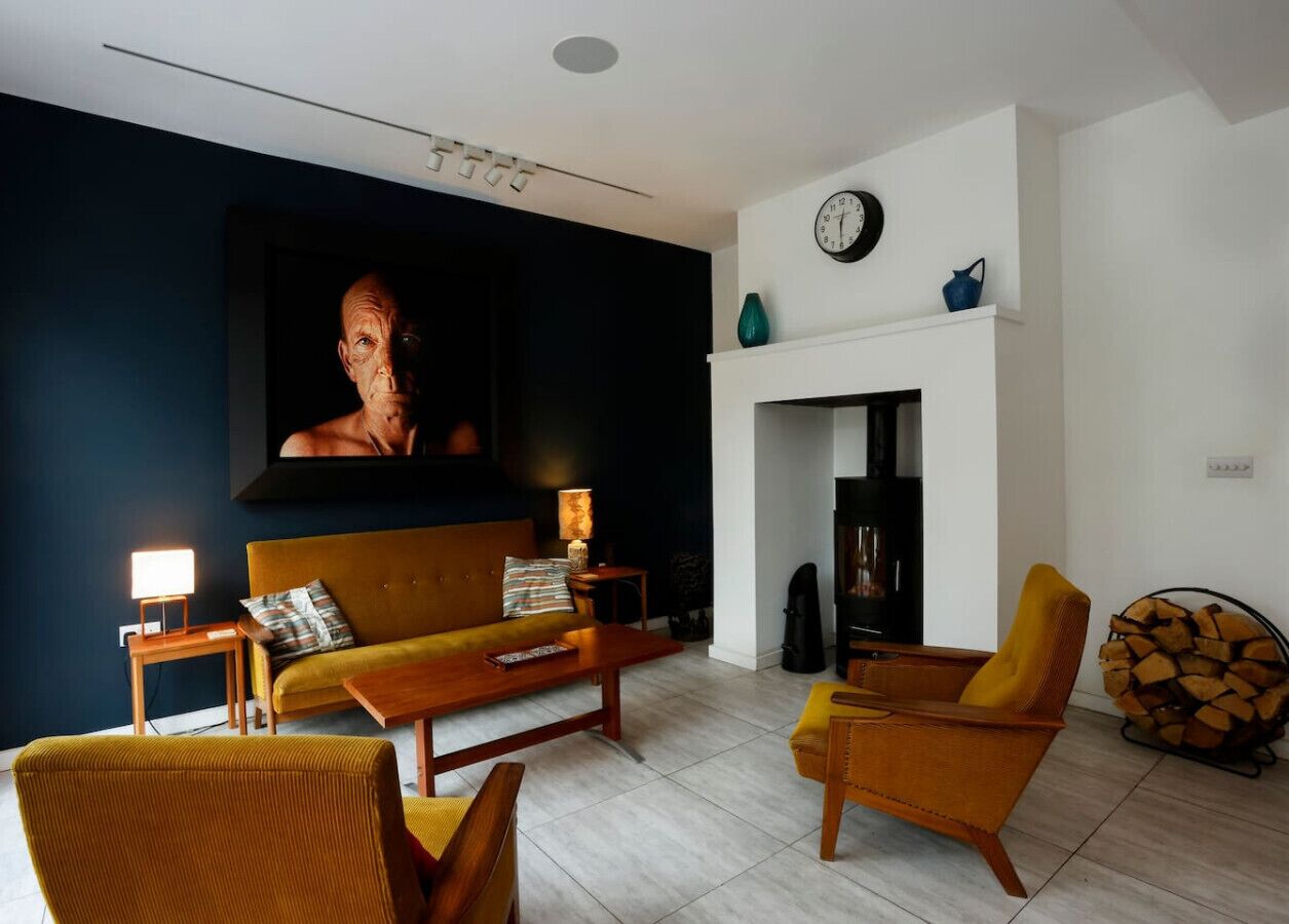 Un salon comprenant un canapé, deux fauteuils, une table basse, une cheminée, une horloge et un téléviseur.