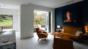 A modern living room with a sofa, armchair, and coffee table. A large window provides a view of the outdoors. - Detached Edwardian Villa with Garden & Parking (Broadstairs)
