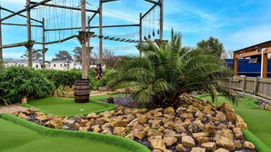 A miniature golf course with a palm tree, rocks, and a wooden bridge. - Phoenix Retreat (Ruan Minor)