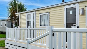 A mobile home with a white deck, a door, and a window. - Phoenix Retreat (Ruan Minor)