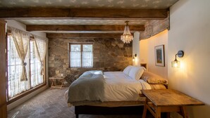 Ein gemütliches Schlafzimmer mit einer Steinwand, einem hölzernen Bettgestell, einem kleinen Holztisch und einer Kristallleuchtre.