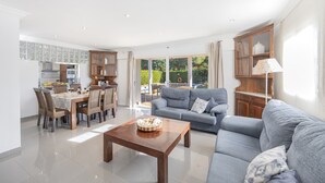 A spacious living area with a dining table, sofa, and kitchen in the background. - House Massanet for 8 with swimming pool near the beach and all amenities (Puerto de Alcudia)