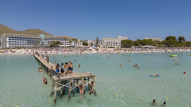 A beach resort with a pier, clear turquoise waters, and a large building with multiple balconies. - House Massanet for 8 with swimming pool near the beach and all amenities (Puerto de Alcudia)