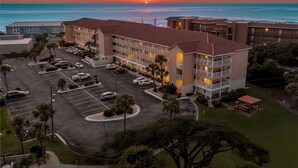 Een hotel met meerdere verdiepingen, een parkeerplaats en uitzicht op de oceaan bij zonsondergang.