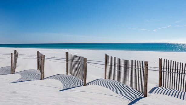 Een zandstrand met houten omheiningen en een helderblauwe lucht.