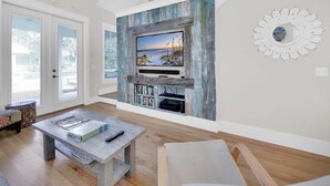 A modern living room with a large flat-screen TV mounted on a rustic wall, a wooden coffee table, and a comfortable seating area. - 🐟2 Pools-4 Bikes-ClaireN'Bea by the Sea (Santa Rosa Beach)