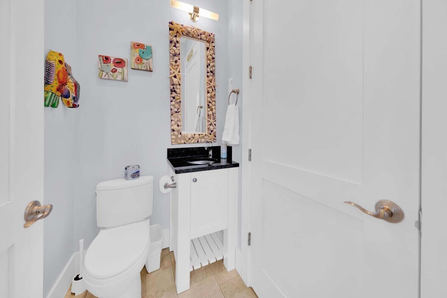 Ein schmales Badezimmer mit Toilette in Weiß, einem Waschbecken mit schwarzer Arbeitsplatte und einem Spiegel mit dekorativem Rahmen.