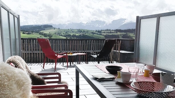 Ein Balkon mit Tisch und Stühlen für zwei Personen und Blick auf eine Berglandschaft.