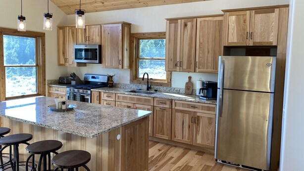 Eine moderne Küche mit Holzausbau, Granitarbeitsplatten, einem Edelstahlkühlschrank und einer Bar mit Hockern.