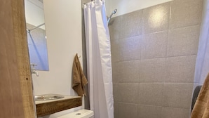 A bathroom with a toilet, a shower with a curtain, a sink, and a towel hanging on the wall. - Willhouse Hostel (Pucón)