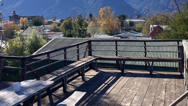 A wooden deck with picnic tables and a metal railing, overlooking a town and mountains. - Willhouse Hostel (Pucón)