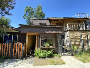 A rustic cabin with a wooden exterior, a balcony, and a fenced yard.
