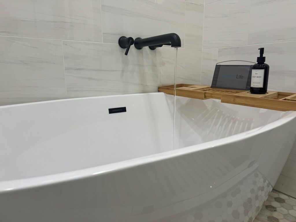 Uma banheira branca com uma torneira preta e uma prateleira de madeira com uma embalagem de gel de banho.