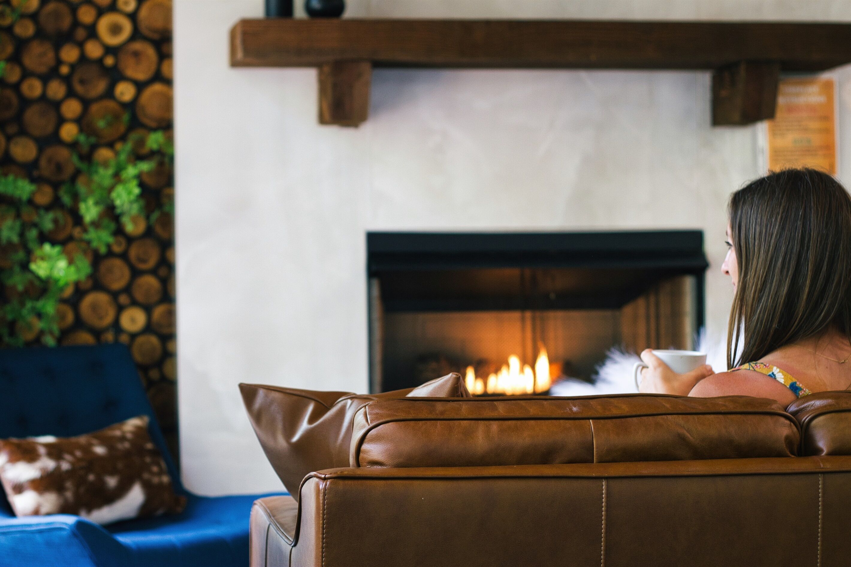 A person sitting on a brown leather sofa facing a fireplace with a visible fire.