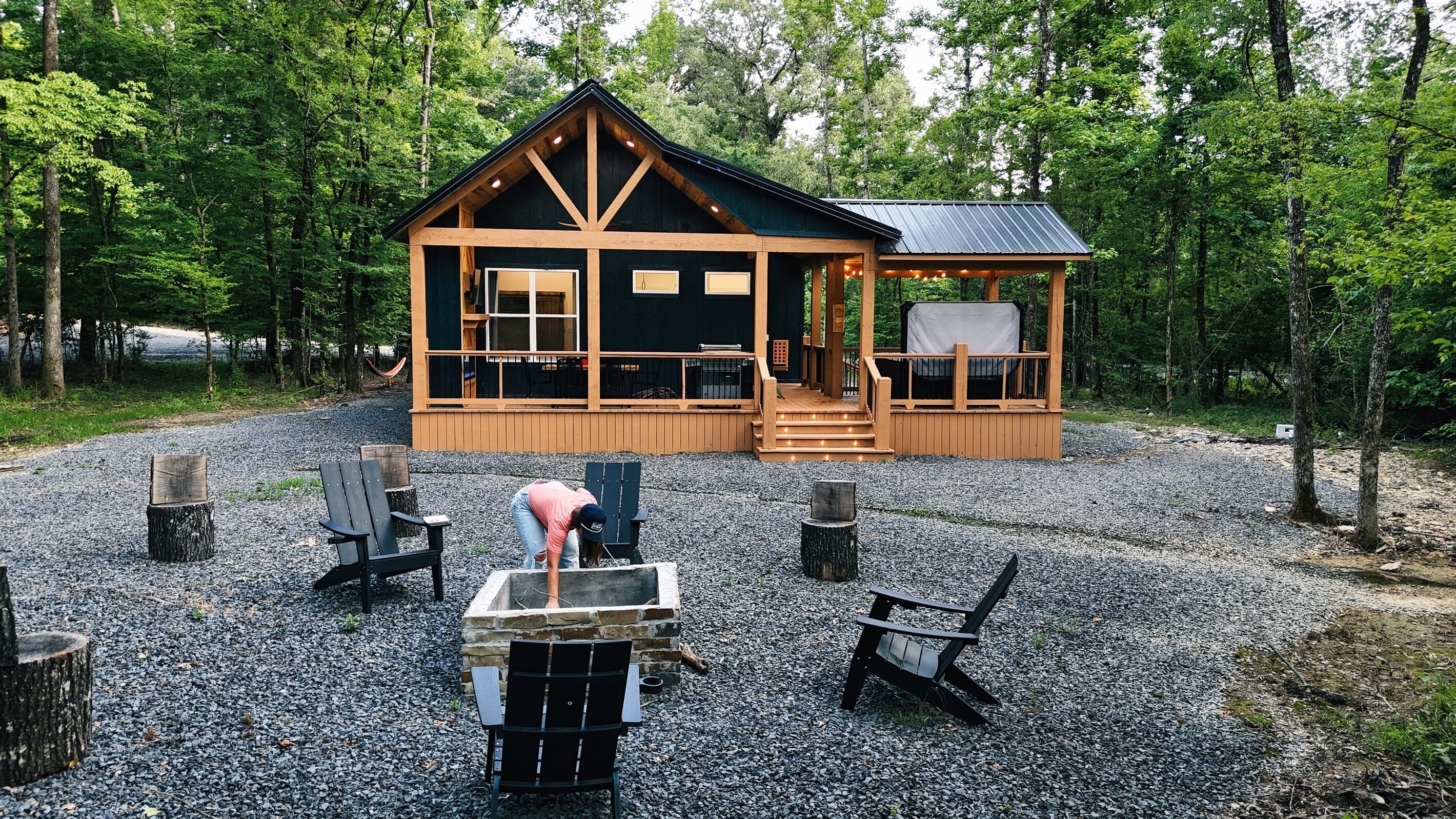 Une cabane dotée d’une véranda, entourée d’arbres, et aménagée avec un espace salon extérieur et un foyer.