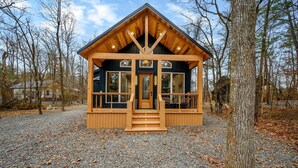 A cabin with a wooden exterior, large windows, and a porch with steps leading to the entrance. - Private Pond | Kayaks · Spa Bath | Romantic Cabin (Broken Bow)