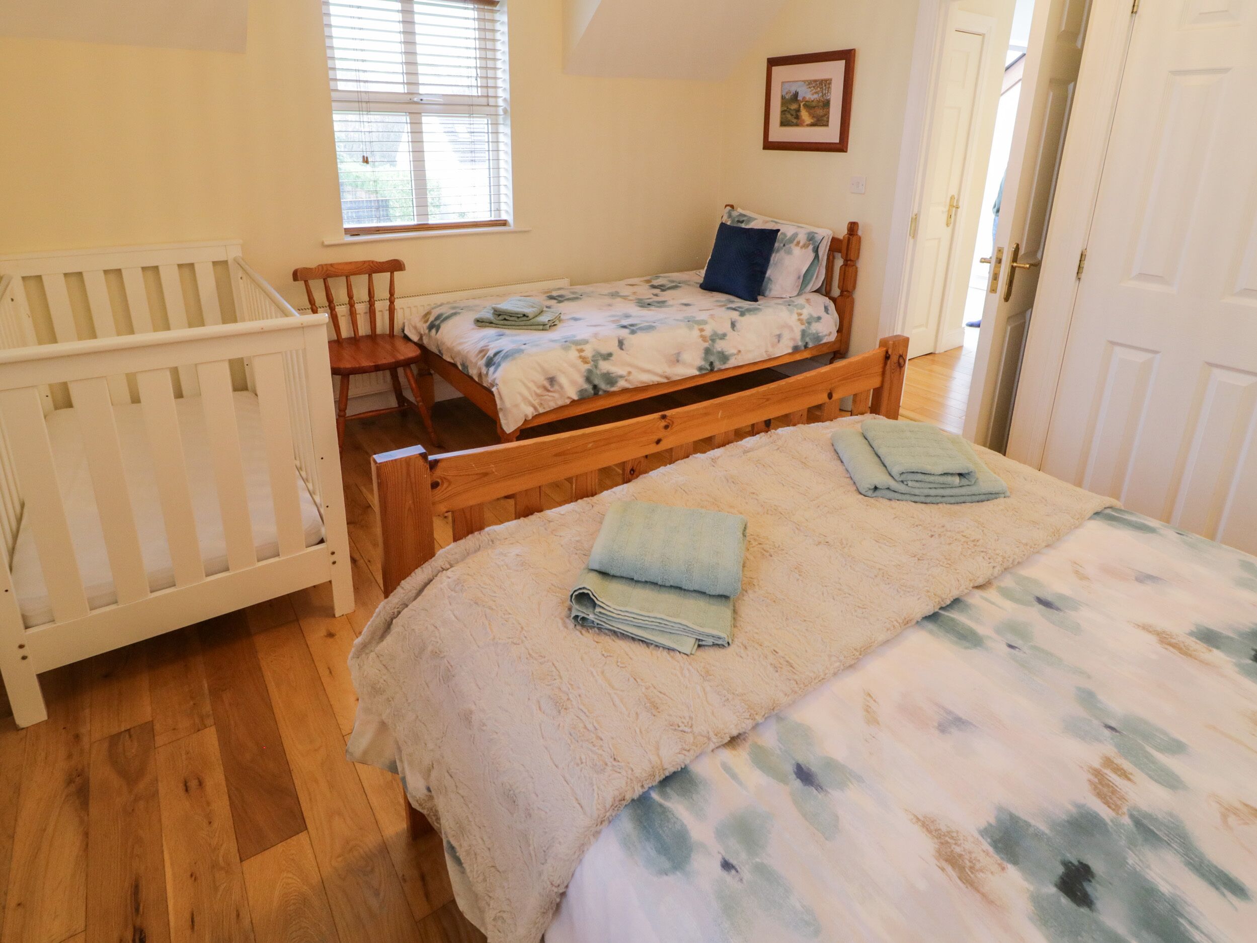 Un dormitorio con cama de madera, una cuna, una ventana y una puerta.
