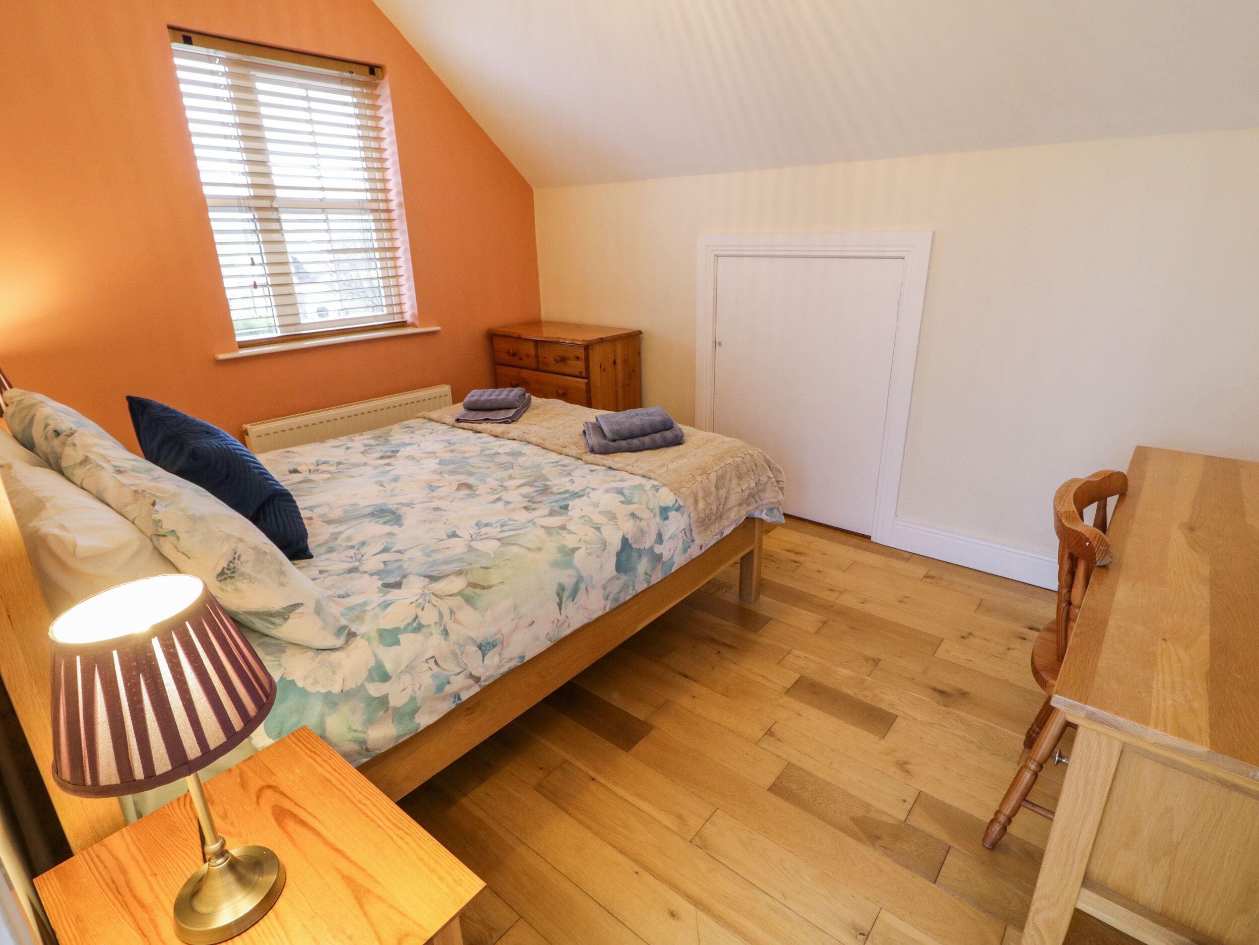 Ein Schlafzimmer mit Bett, Nachttisch, Holzstuhl, Schreibtisch und Fenster mit Jalousien.