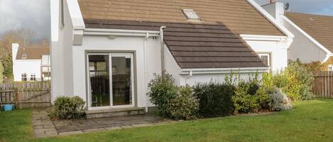 A residential house with a sloped roof, a sliding glass door, and a small garden area.