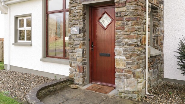 Une maison aux murs recouverts de pierres, avec une porte rouge, une boîte aux lettres et une plaque de numéro de maison.