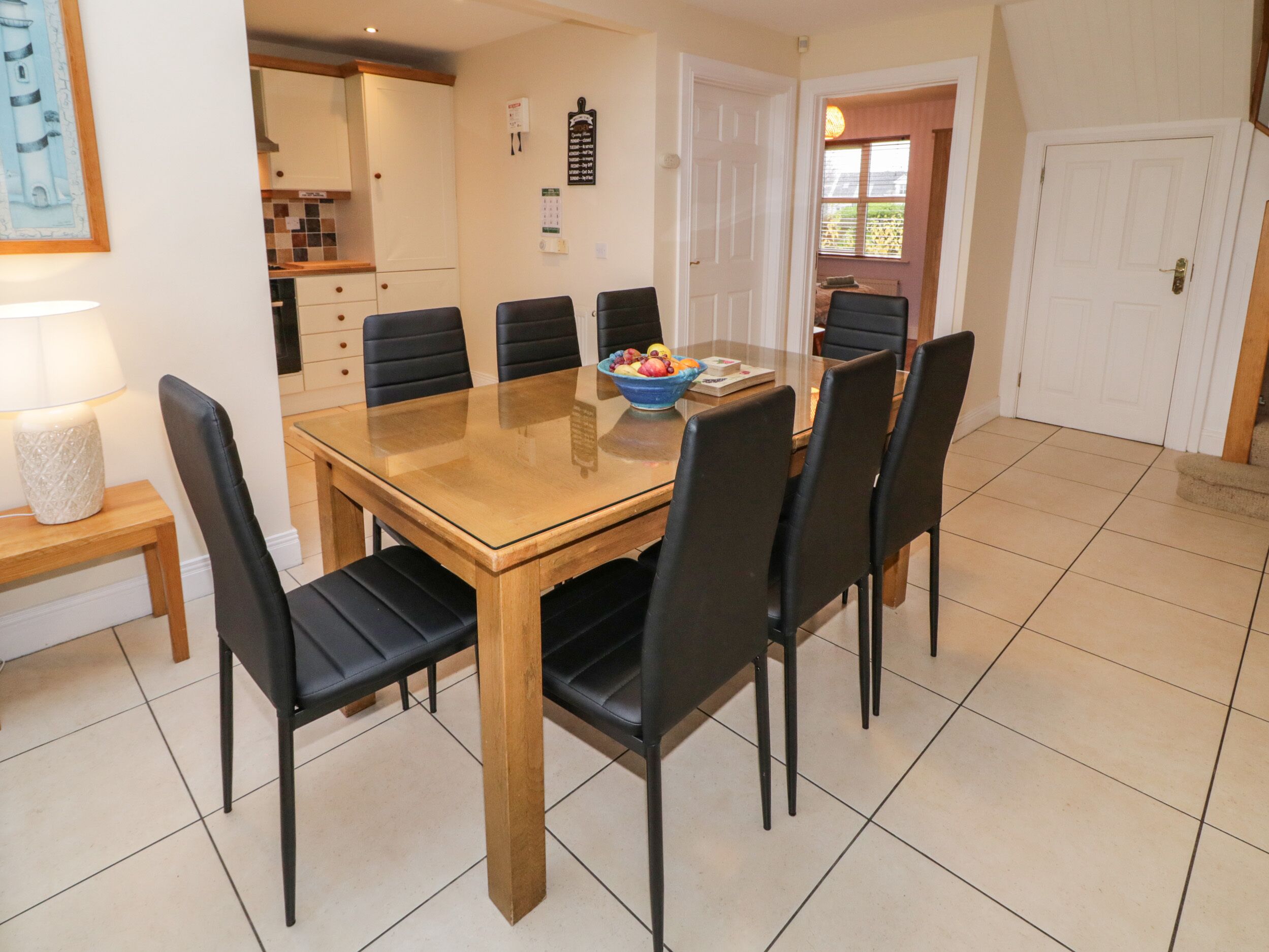 A dining area with a wooden table and black chairs, a bowl of fruit, and a lamp on a side table.