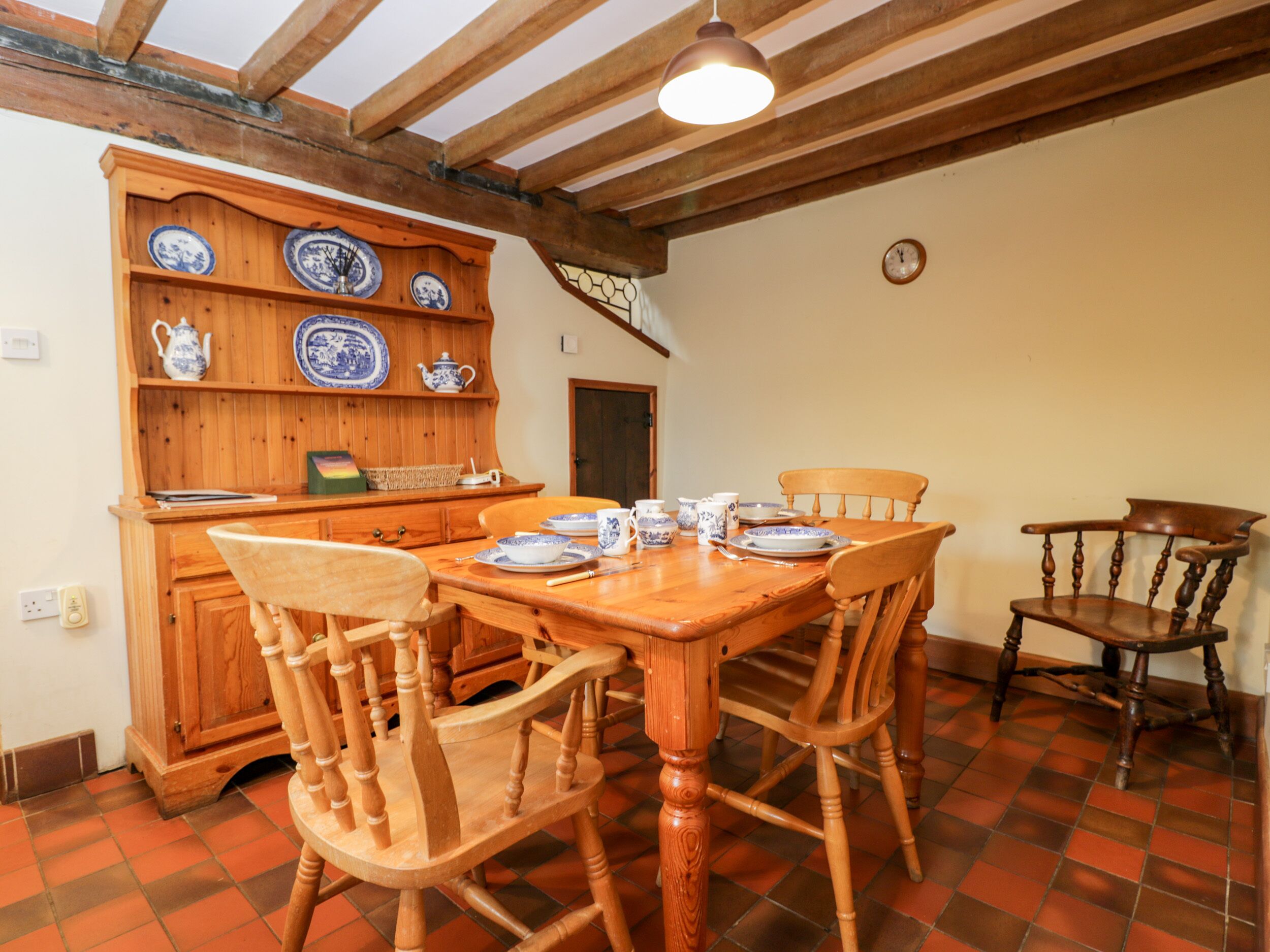 Un comedor con una mesa y sillas de madera, un armario de madera con platos azules y blancos, y un reloj en la pared.