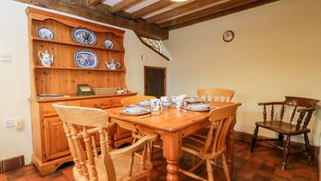 Un comedor con una mesa y sillas de madera, un armario de madera con platos azules y blancos, y un reloj en la pared.