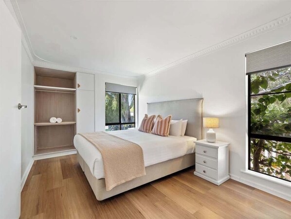 A bedroom with a bed, bedside table, and a window with a view of greenery.