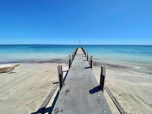 A pier leading to a beach with clear blue water and a sandy shore.