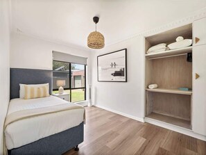 A bedroom with a bed, a bedside table, a window, a wall-mounted shelf, and a hanging light fixture.