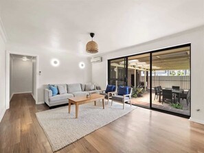A modern living room with a sofa, coffee table, and chairs, a large sliding glass door leading to an outdoor patio. - Bluewater Retreat - Pet-Friendly Coastal Oasis (Broadwater)