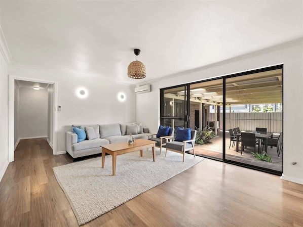 A modern living room with a sofa, coffee table, and chairs, a large sliding glass door leading to an outdoor patio.