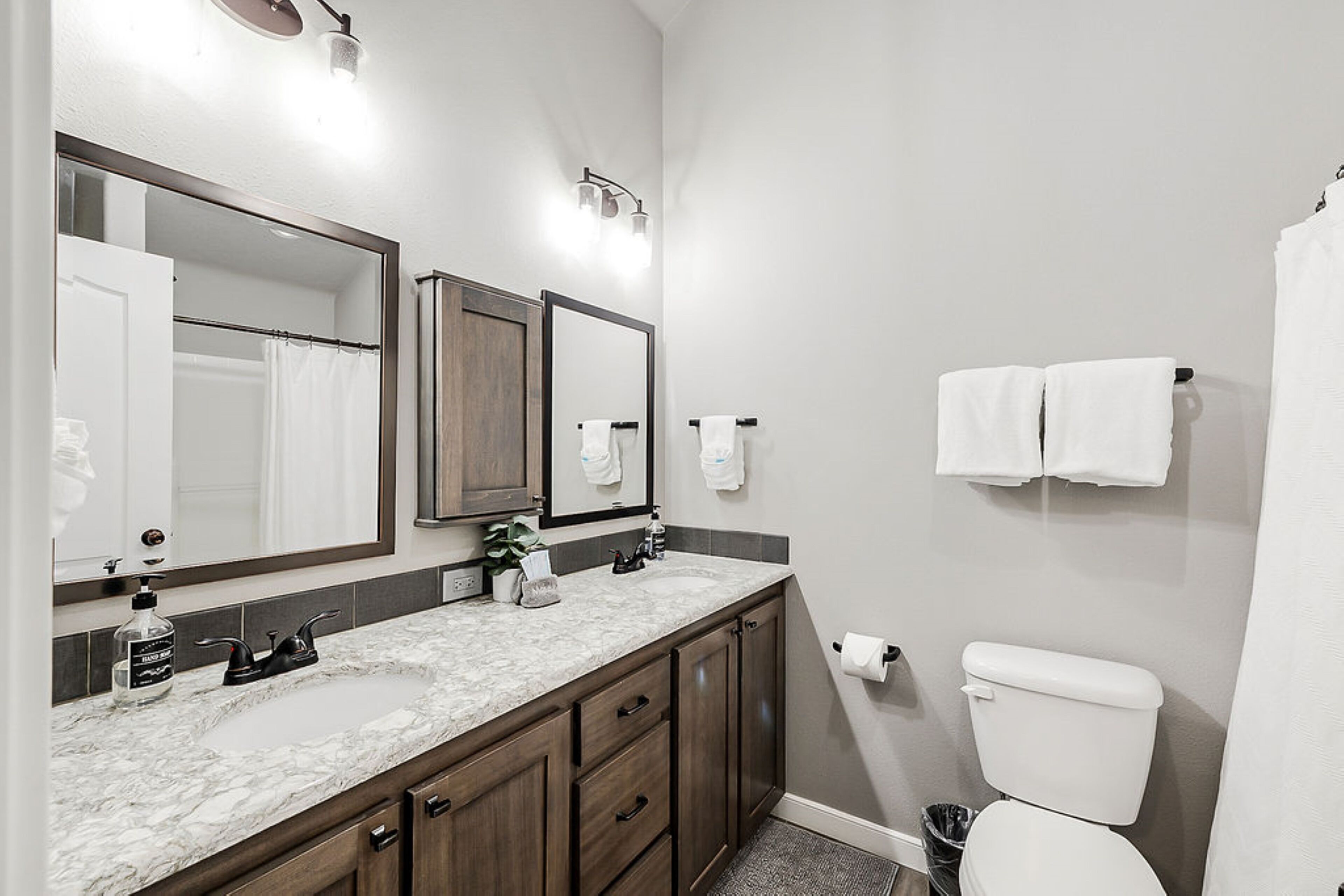 A modern bathroom with a double sink, a large mirror, a toilet, and a shower curtain.