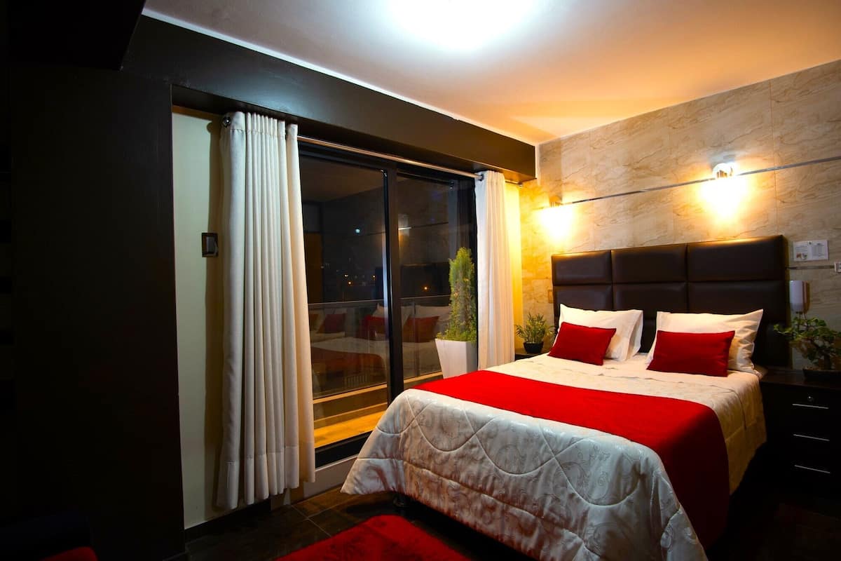 A modern bedroom with a large bed, a sliding glass door to a balcony, and a stone wall.