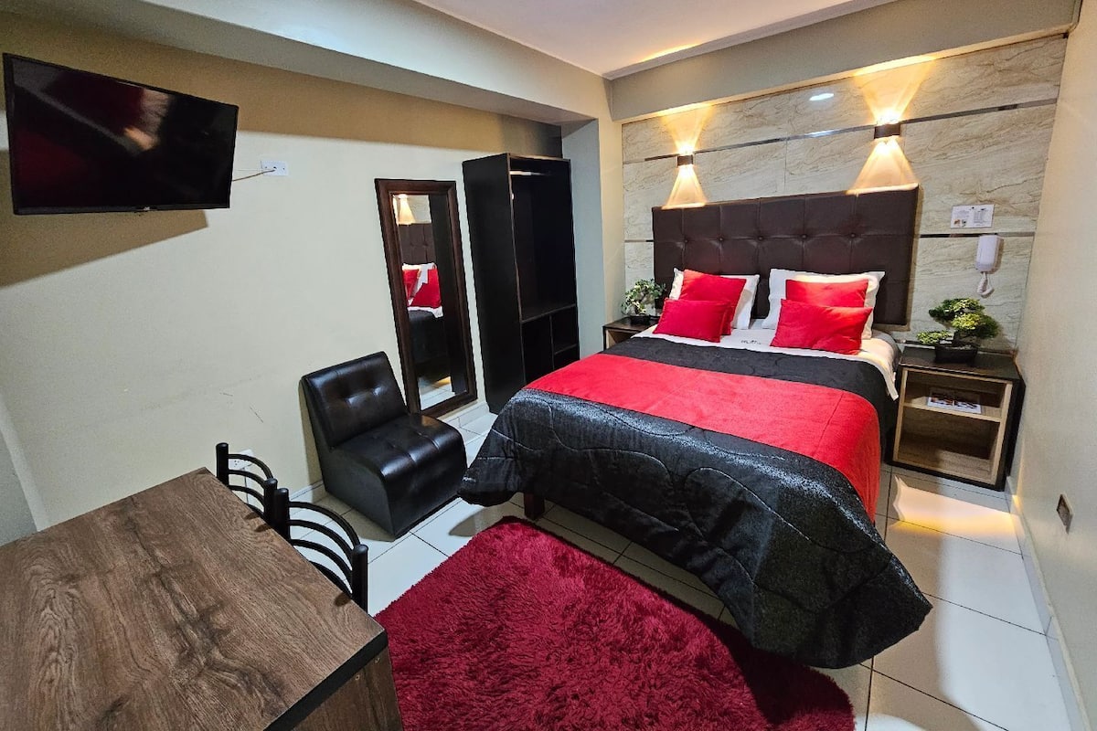 A modern hotel room with a large bed, a TV mounted on the wall, a desk, and a chair.