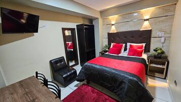 Una habitación de hotel moderna con una cama grande, un televisor montado en la pared, un escritorio y una silla.