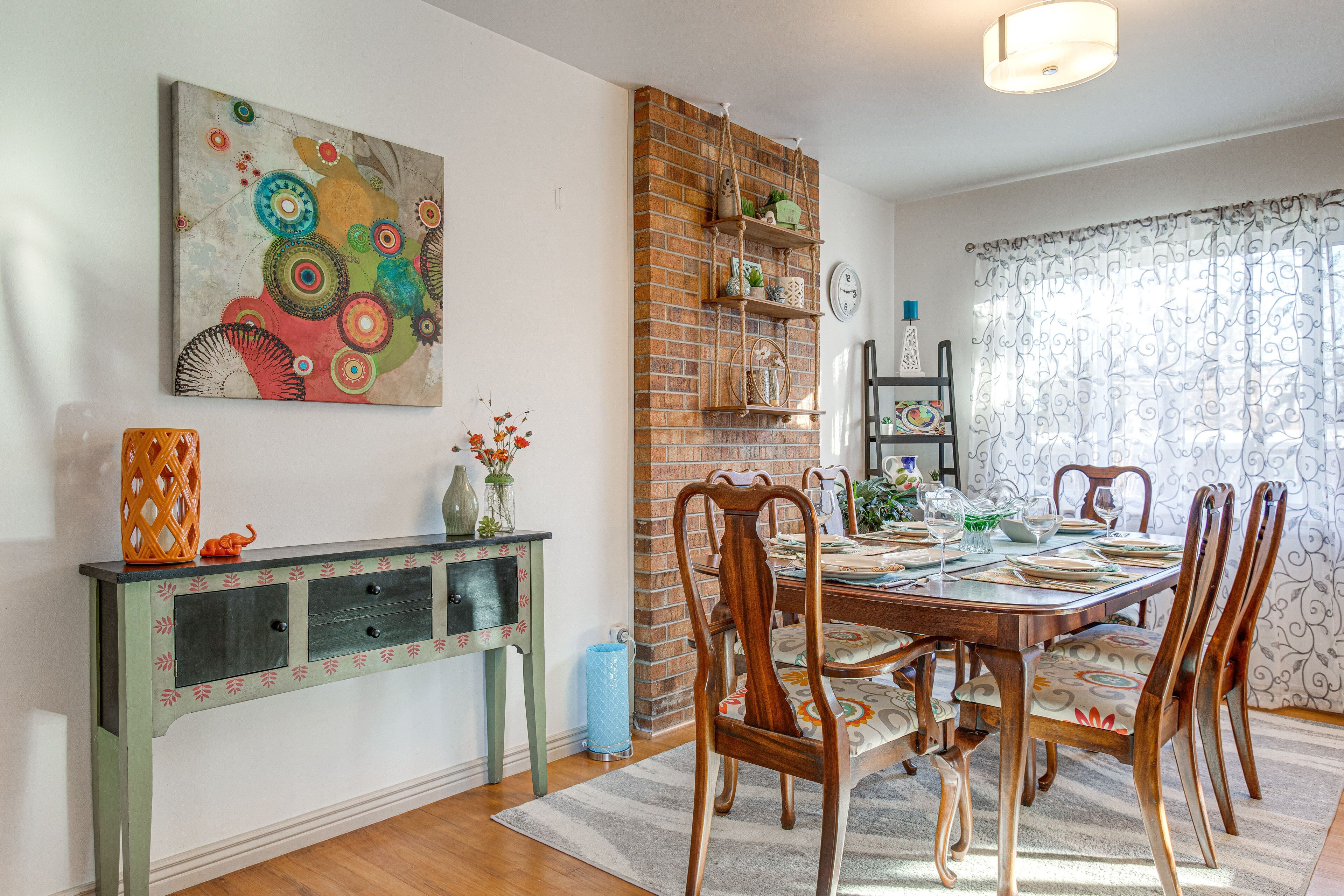 A dining area with a brick wall, wooden chairs, a table set for four, and a decorative painting on the wall.