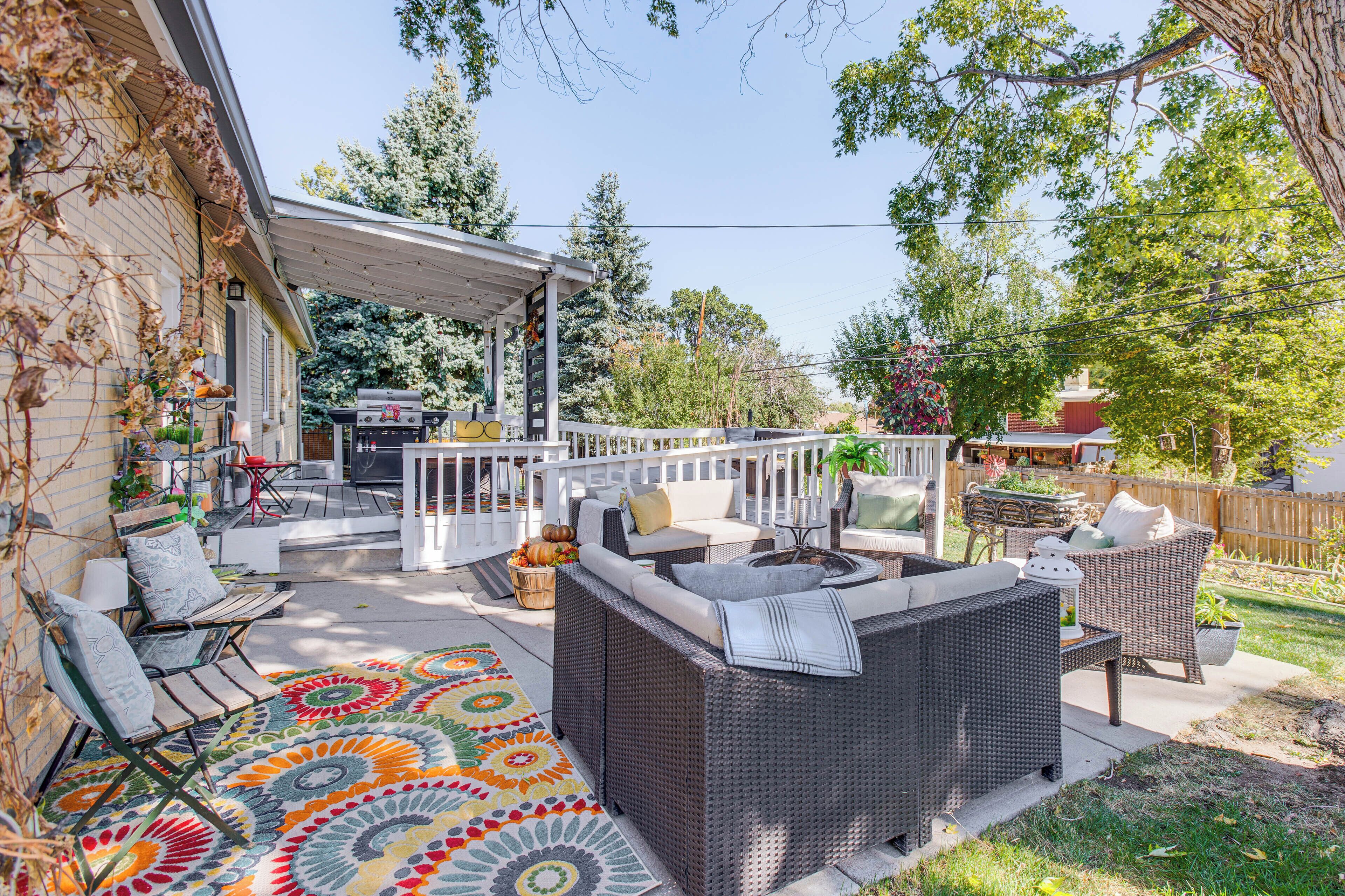 Un patio al aire libre con mobiliario de mimbre, una alfombra colorida y una parrilla para barbacoa.