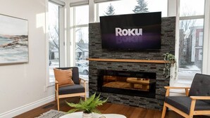 Een moderne woonkamer met een stenen openhaard, een flatscreen televisie erboven en twee fauteuils.