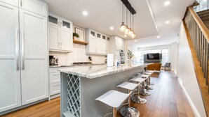 Een moderne keuken met witte kastjes, een marmeren eiland en barstoelen.