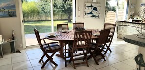 A dining area with a round wooden table and six chairs, a view of a grassy garden through large windows, and a wall with marine life illustrations.