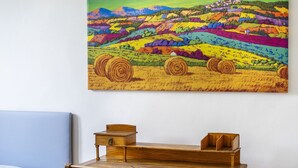 A wooden desk with drawers and a chair, a blue pillow, and a colorful landscape painting on the wall. - Servi 39 - Innocenti (Firenze)