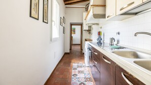 A narrow kitchen with a tiled backsplash, wooden cabinets, and a tiled floor leading to a doorway. - Servi 39 - Innocenti (Firenze)