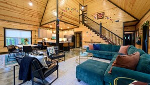 A spacious living area with a high ceiling, wooden walls, a staircase, and a dining area.